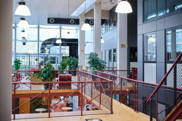 Moderne en lichte kantoorlounge aan het John M. Keynesplein met rode balustrades, planten en zithoeken.
