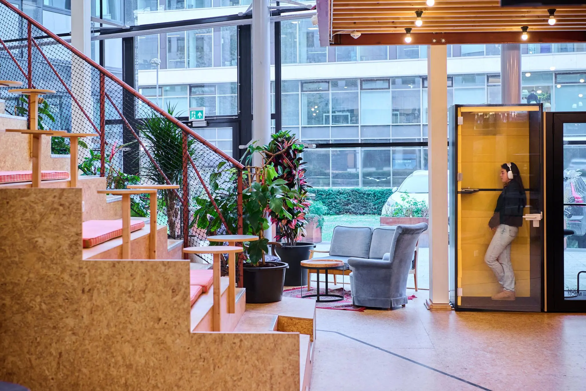 Moderne en kleurrijke kantoorlounge aan het John M. Keynesplein met zittribune, planten en een stille belcel met een vrouw erin.