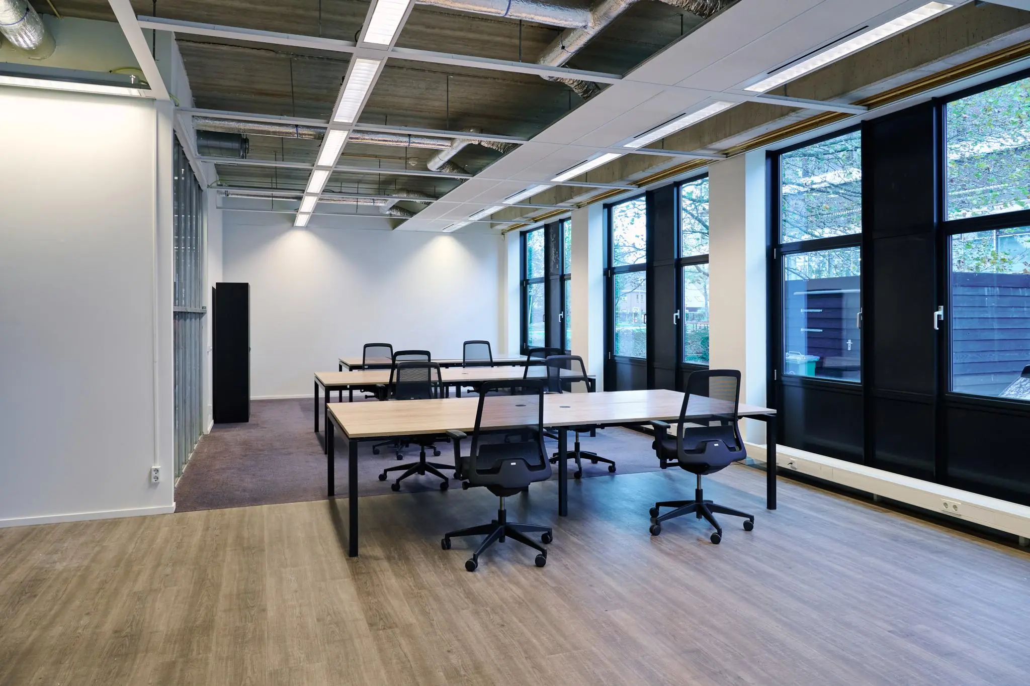 Moderne open kantoorruimte aan het John M. Keynesplein met bureaus en ergonomische stoelen bij grote ramen.