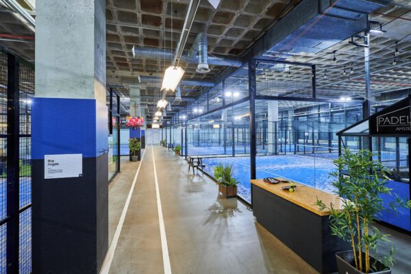 Indoor padelcentrum op het John M. Keynesplein in Amsterdam met meerdere blauwe padelbanen en een moderne industriële inrichting.