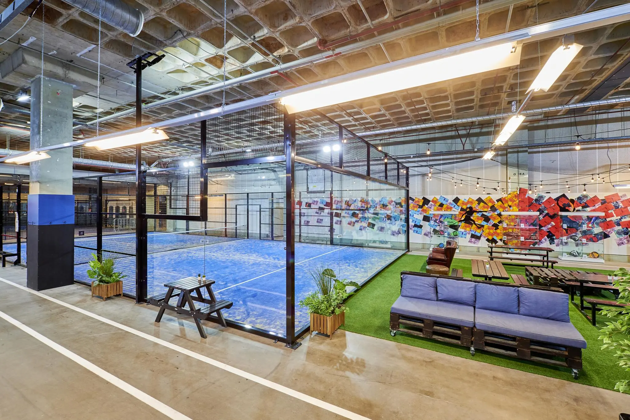 Een modern indoor padelveld op het John M. Keynesplein met naastgelegen zithoek en kleurrijke muurschildering.