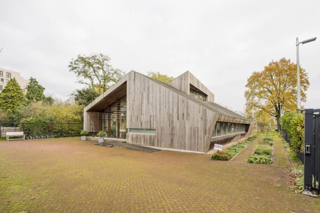 Modern houten gebouw met schuine lijnen aan de Vogelvlinderweg, omgeven door groen en bestrating.