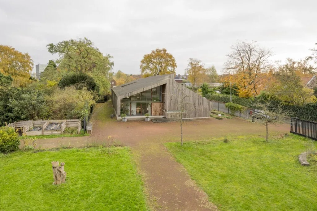 Houten gebouw aan de Vogelvlinderweg, omgeven door groen en herfstbomen, met een modern, schuingeplaatst dak.