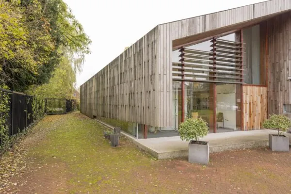Modern houten gebouw aan de Vogelvlinderweg met grote ramen en plantenbakken op een met mos begroeide bestrating.