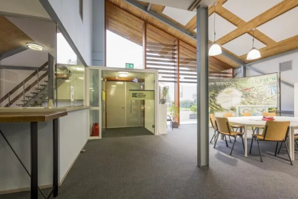 Moderne ontvangstruimte van het kantoor aan de Vogelvlinderweg met glazen ingang, zithoek en informatiepanelen over stedelijke projecten.