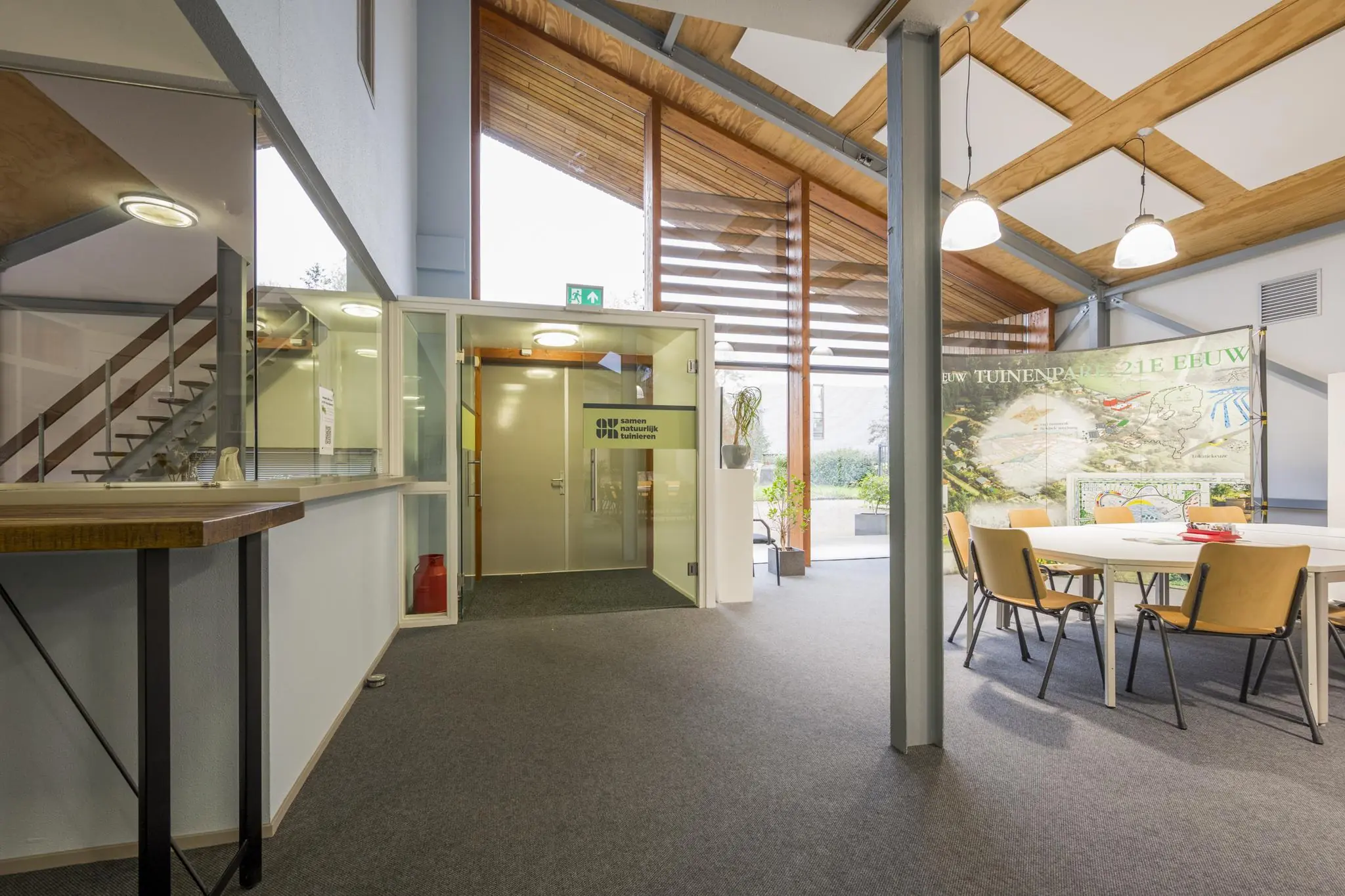 Moderne ontvangstruimte van het kantoor aan de Vogelvlinderweg met glazen ingang, zithoek en informatiepanelen over stedelijke projecten.