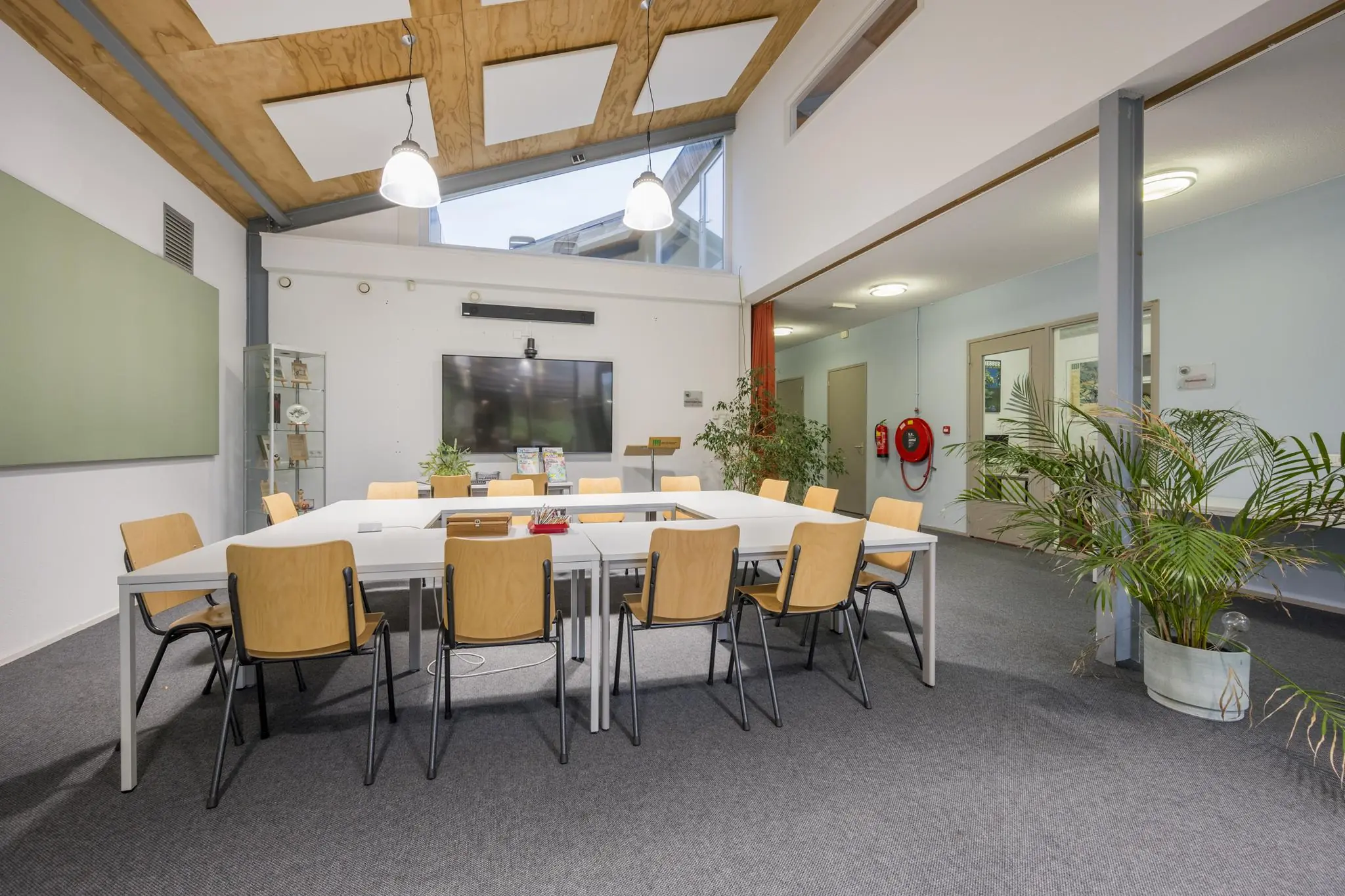 Vergaderruimte met moderne inrichting, houten stoelen rond witte tafels en een groot presentatiescherm aan de muur in een gebouw aan de Vogelvlinderweg.