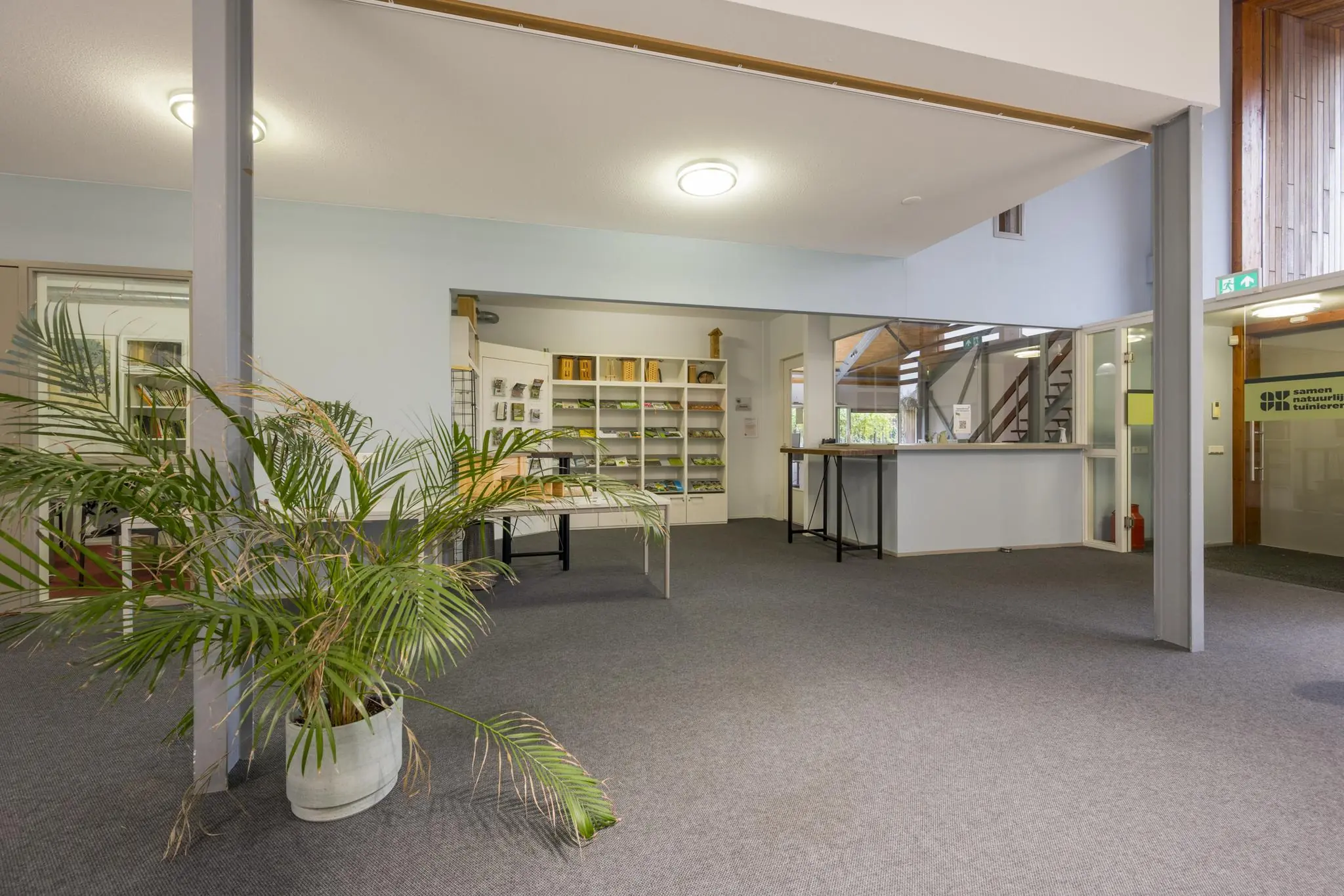 Informatieve entreehal met balie, folderrekken en een grote kamerplant in het gebouw aan de Vogelvlinderweg.