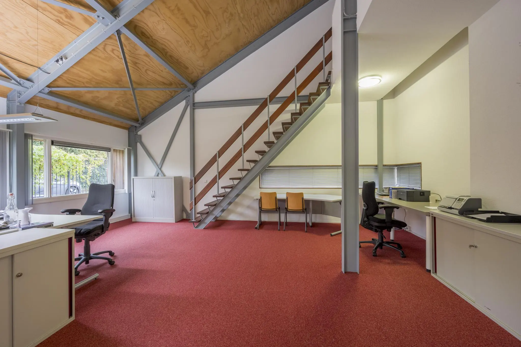 Modern kantoorinterieur aan de Vogelvlinderweg met rood tapijt, schuine houten plafondconstructie en open trap naar entresol.