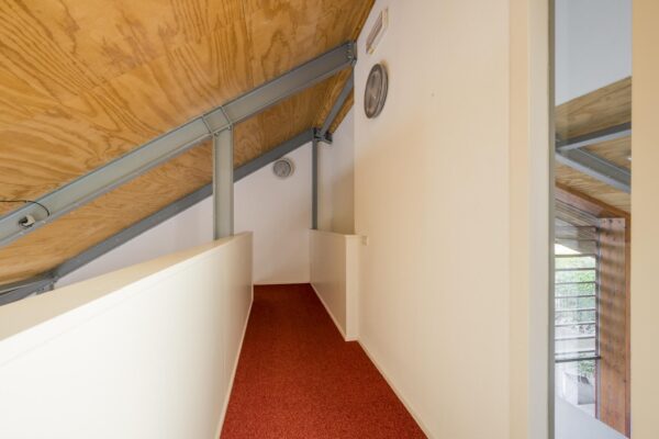 Smalle gang met rood tapijt, schuine houten plafondpanelen en metalen draagbalken in een modern huis aan de Vogelvlinderweg.