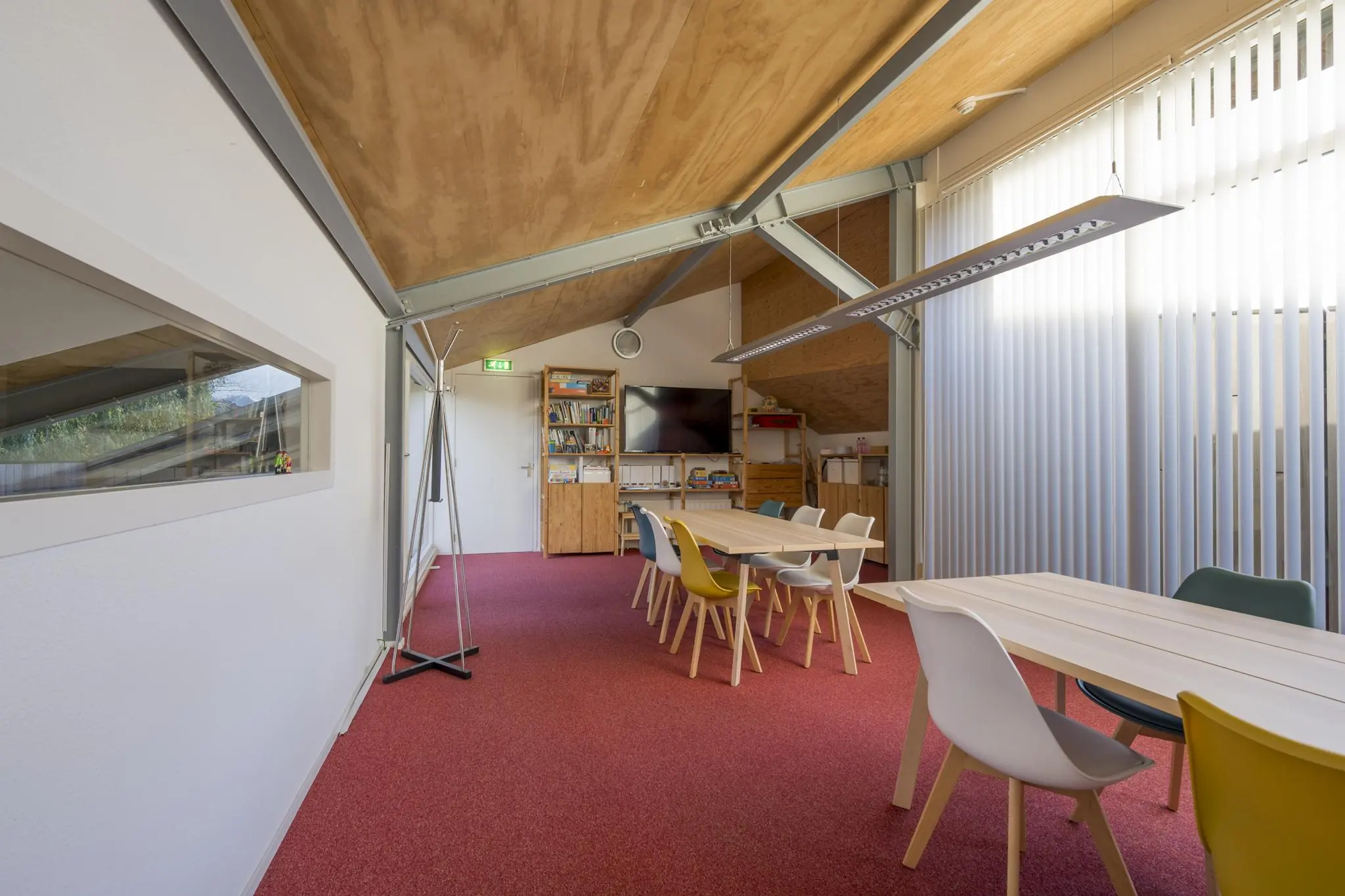 Vergaderruimte aan de Vogelvlinderweg met houten tafels, kleurrijke stoelen, een boekenkast en een flatscreen-tv.