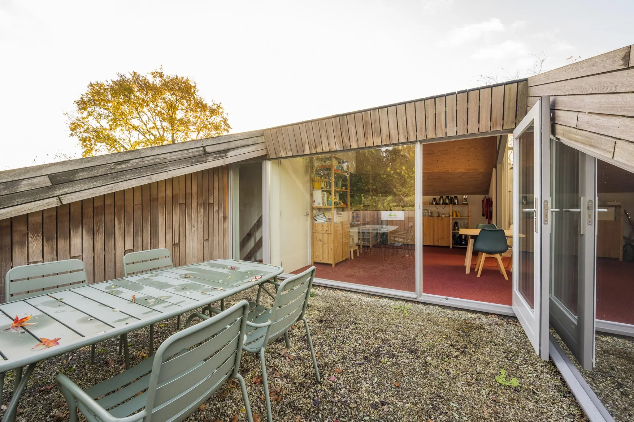 Terras met metalen tuinset en uitzicht op een houten huis met schuine gevel en grote glazen schuifdeuren aan de Vogelvlinderweg.