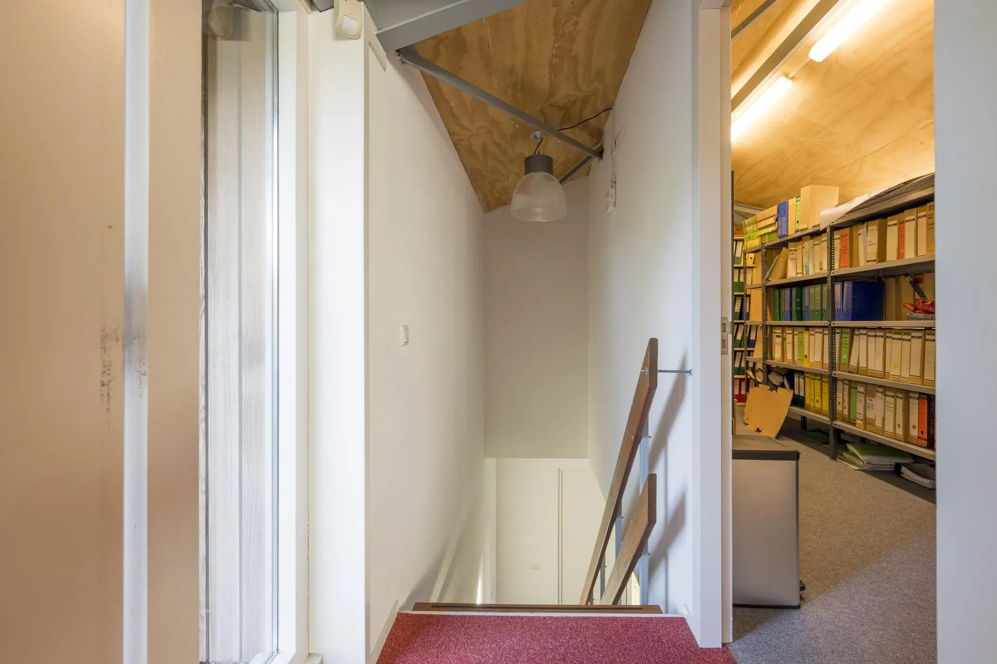 Trapopgang met rode vloerbedekking naast een kantoorarchief vol ordners en documenten in Vogelvlinderweg 173.