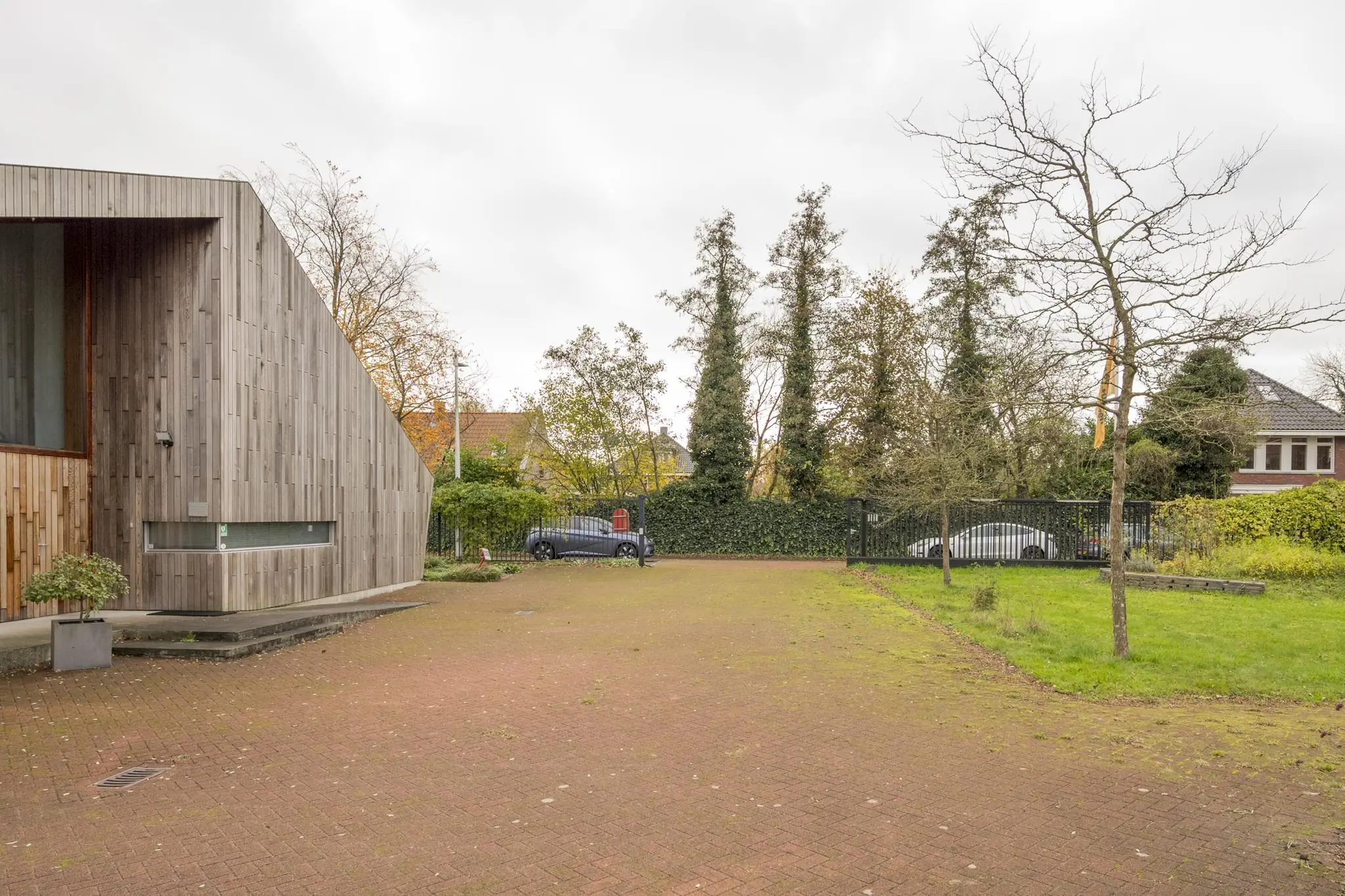 Moderne woning met houten gevel aan de Vogelvlinderweg, met zicht op de oprit en geparkeerde auto's bij een groene erfafscheiding.