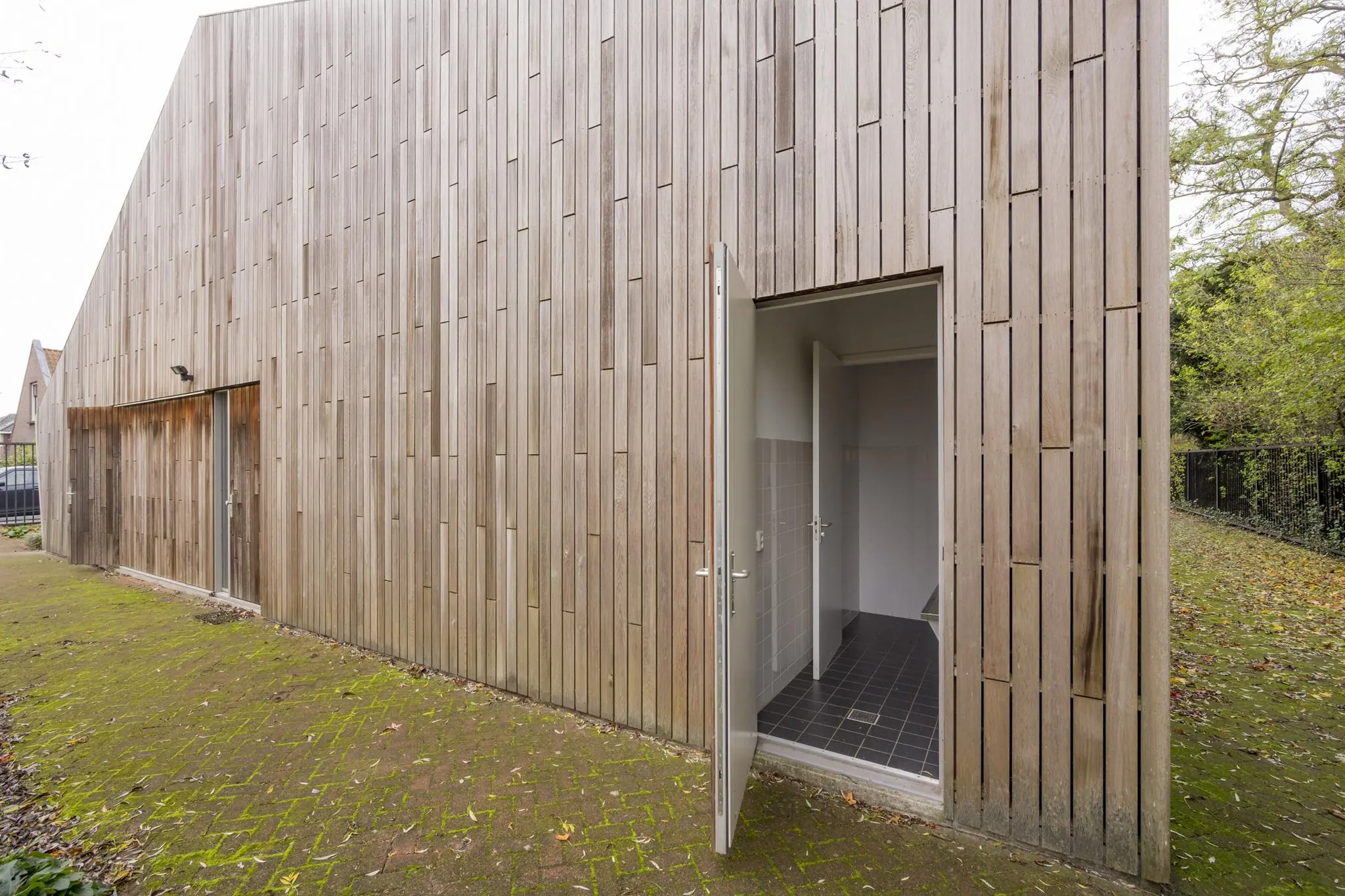 Houten gevel van een modern gebouw aan de Vogelvlinderweg met een open deur naar een betegelde binnengang.