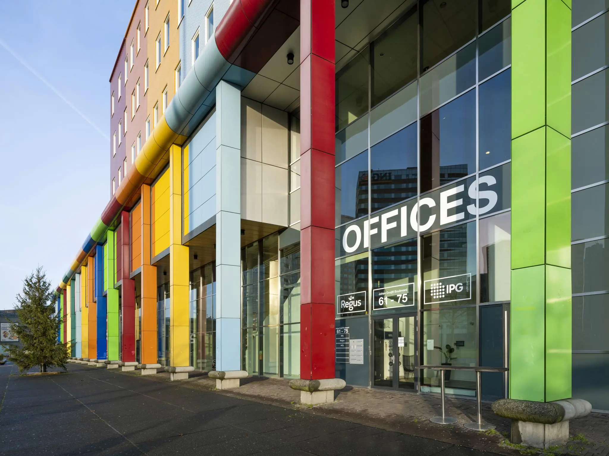 Ingang van een kleurrijk kantoorgebouw aan de Johan Cruijff Boulevard met grote glazen gevel en de tekst "OFFICES".
