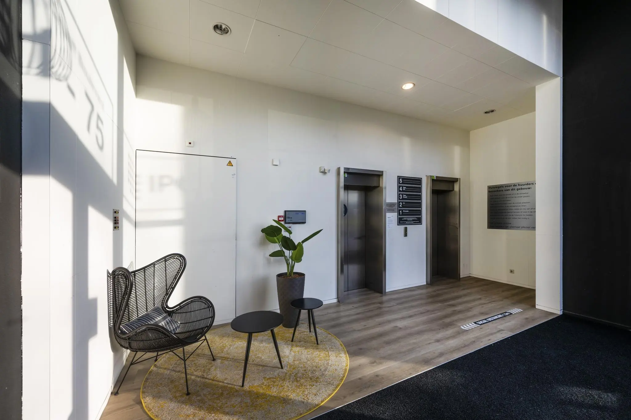 Moderne wachtruimte met zitgedeelte en twee liften in een gebouw aan de Johan Cruijff Boulevard.