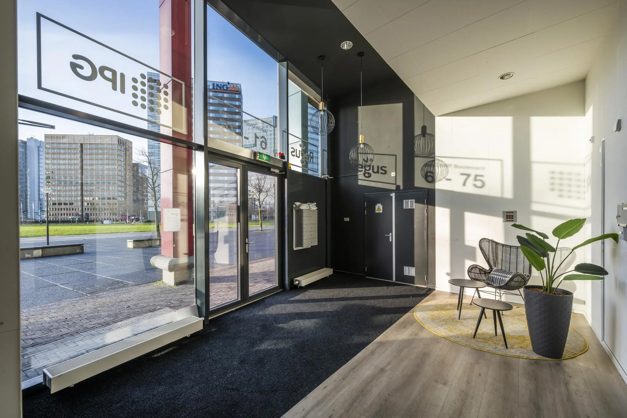 Moderne entreehal aan de Johan Cruijff Boulevard met zitgedeelte, hoge ramen en uitzicht op kantoorgebouwen.