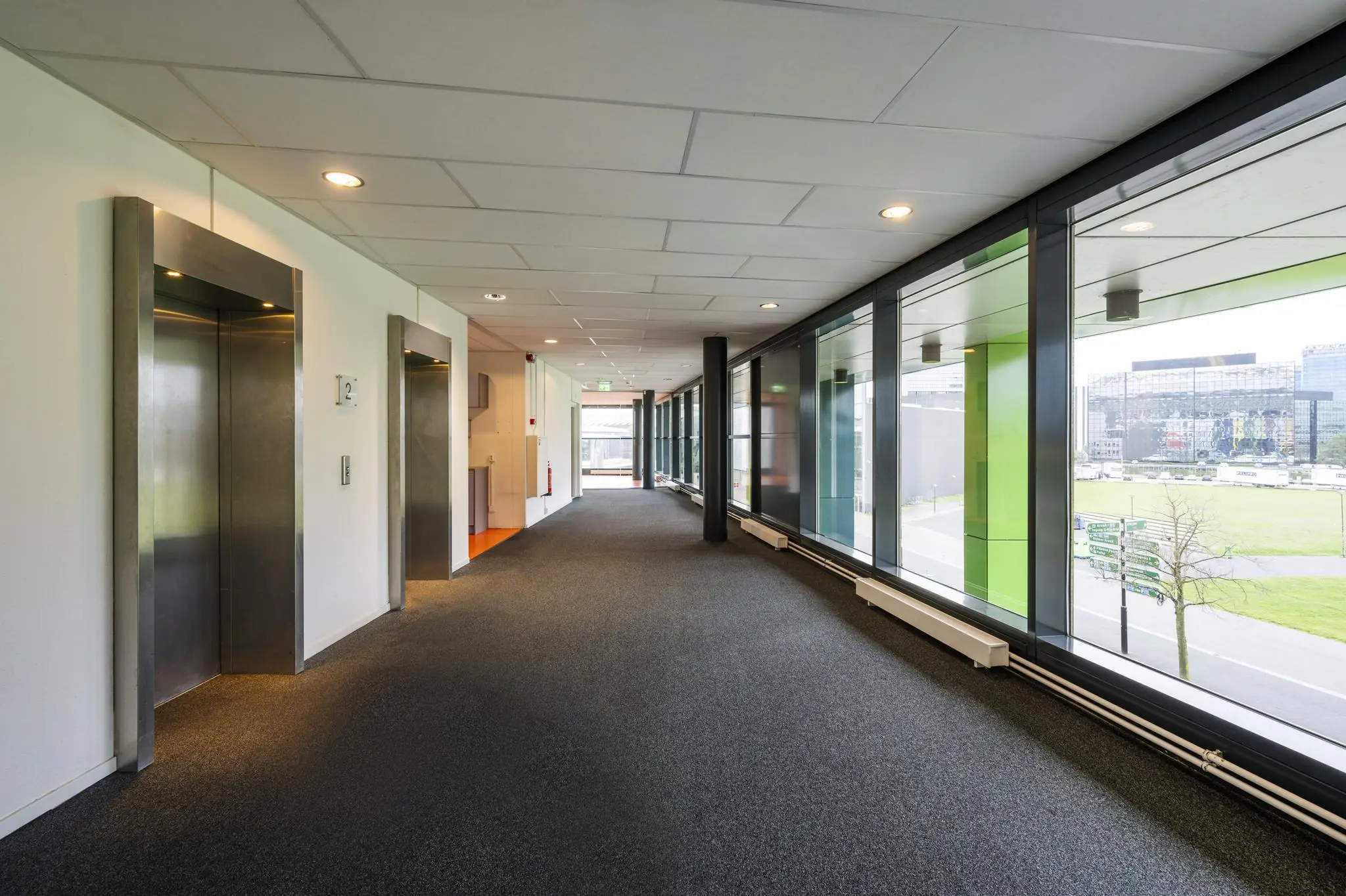 Gang met liften en grote ramen met uitzicht op de Johan Cruijff Boulevard in Amsterdam.