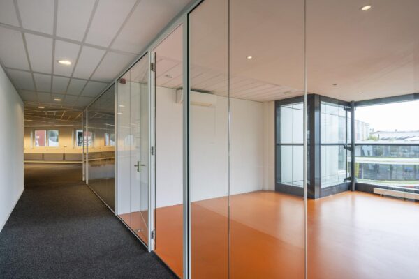 Lichte kantoorruimte met glazen wanden en oranje vloer aan de Johan Cruijff Boulevard.