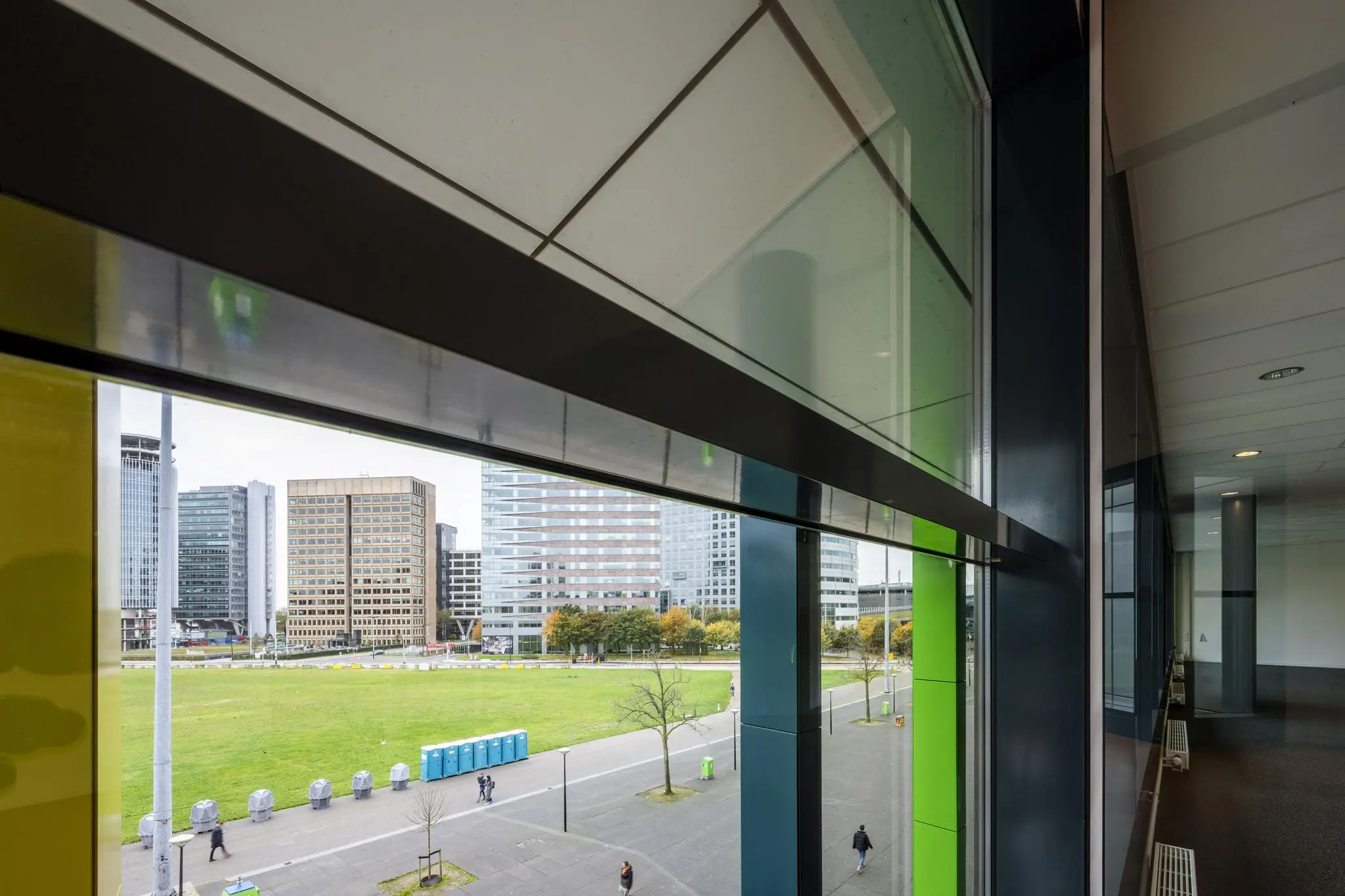 Uitzicht vanuit een modern kantoorgebouw op de Johan Cruijff Boulevard met grasveld, hoogbouw en passerende voetgangers.