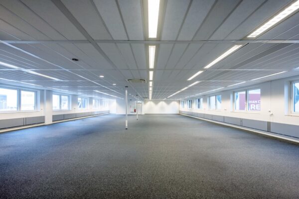 Licht, leeg kantoor met tapijtvloer en grote ramen aan de Johan Cruijff Boulevard.
