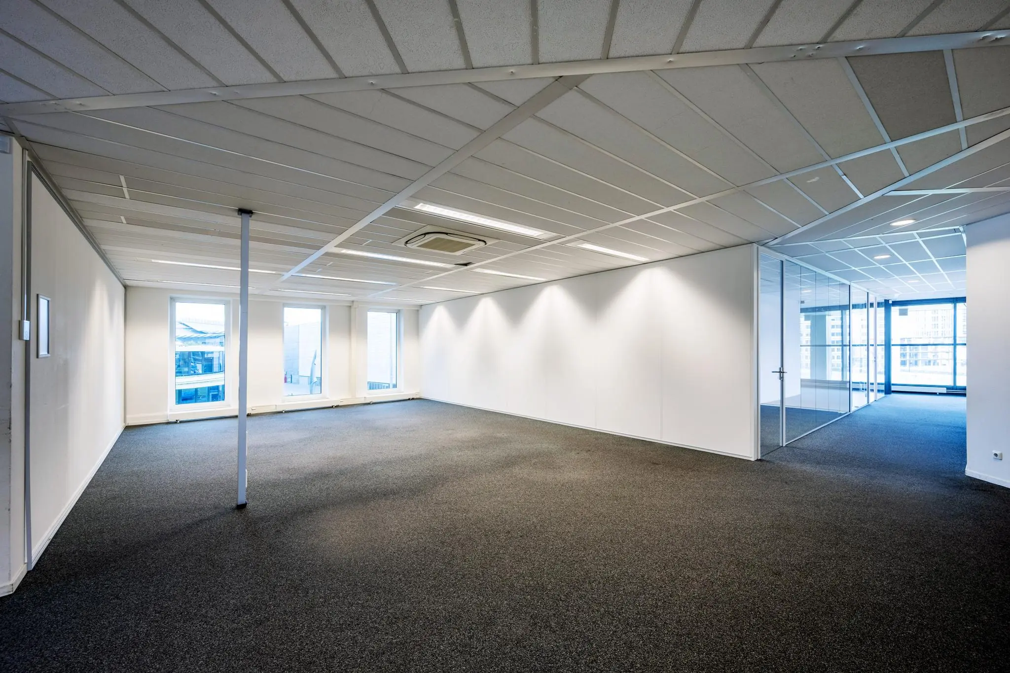 Leeg kantoorpand aan de Johan Cruijff Boulevard met witte wanden, systeemplafond en glazen vergaderruimte.