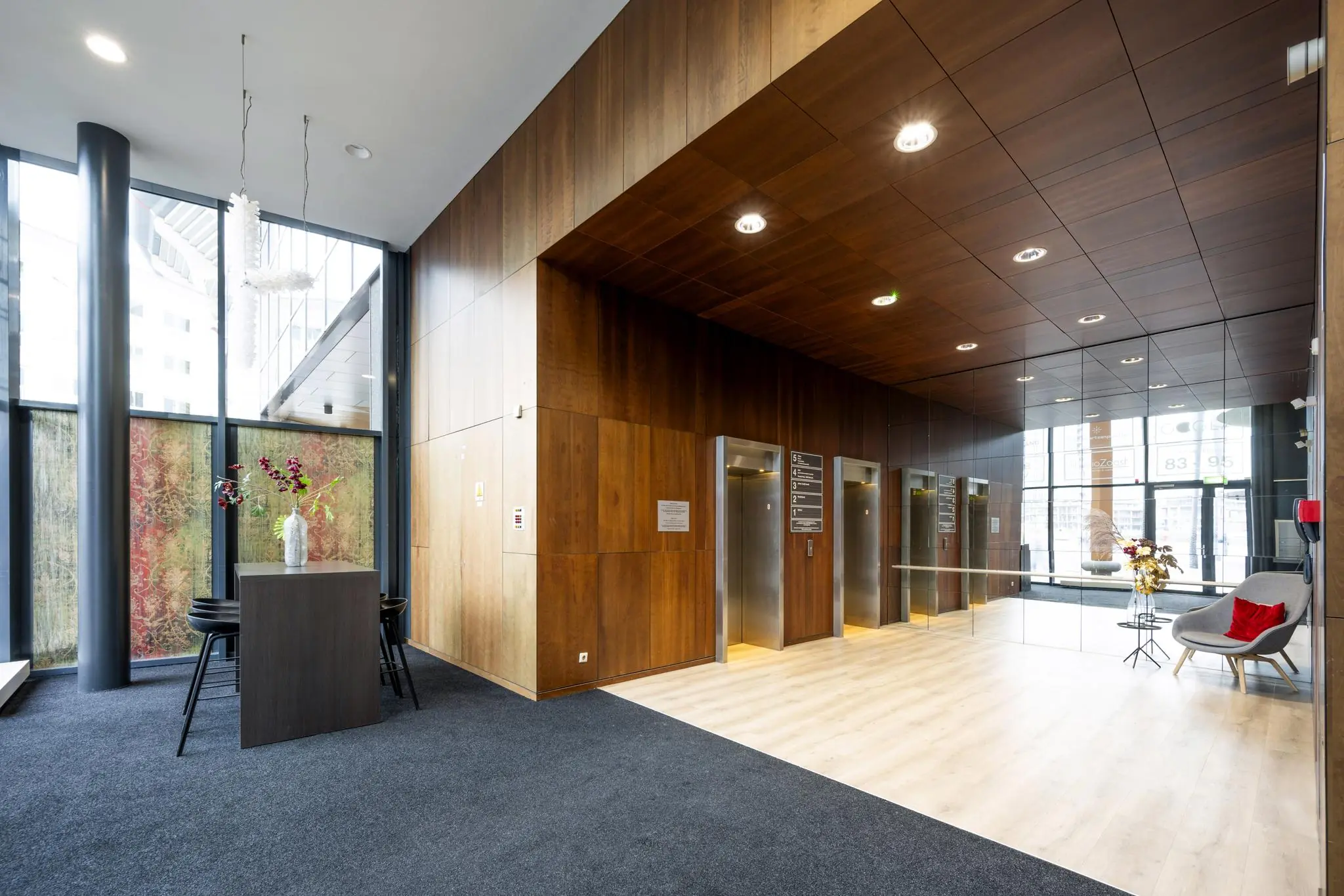 Moderne entreehal aan de Johan Cruijff Boulevard met houten wandafwerking, drie liften en stijlvolle wachthoek.