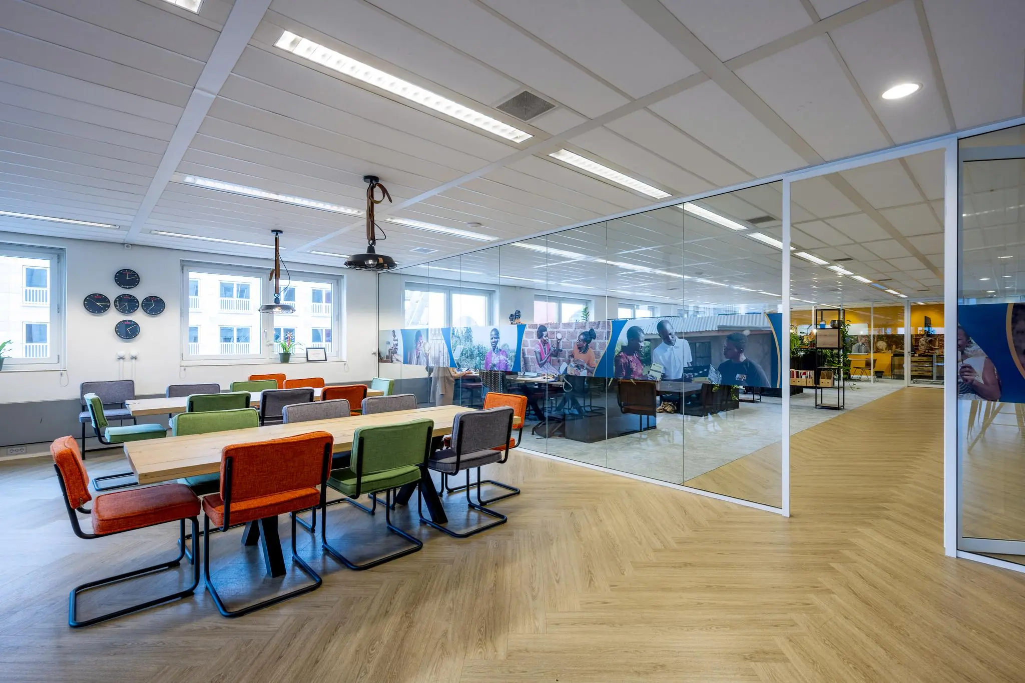 Moderne vergaderruimte aan de Johan Cruijff Boulevard met kleurrijke stoelen, houten vloer en glazen wand met fotoprint.