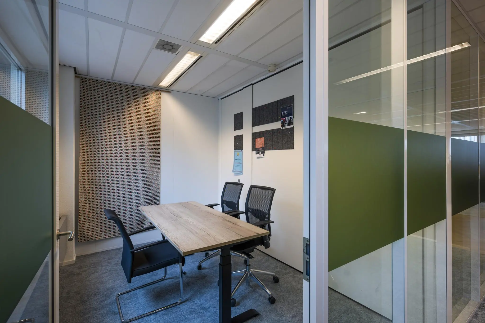 Kleine vergaderruimte aan de Johan Cruijff Boulevard met glazen wanden, een houten tafel en drie bureaustoelen.