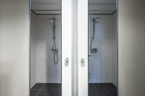 Twee aangrenzende doucheruimtes met witte betegeling en moderne douchekoppen in een sportaccommodatie aan de Johan Cruijff Boulevard.