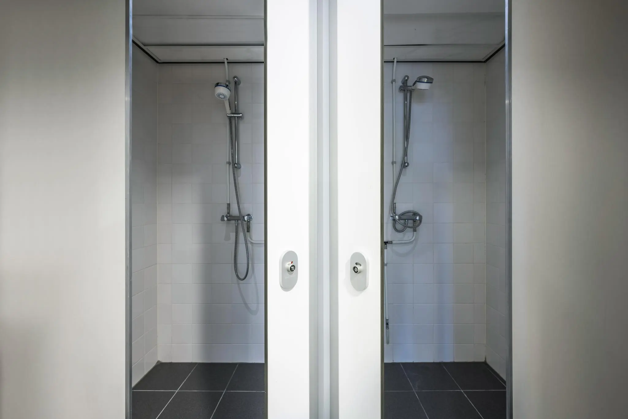 Twee aangrenzende doucheruimtes met witte betegeling en moderne douchekoppen in een sportaccommodatie aan de Johan Cruijff Boulevard.