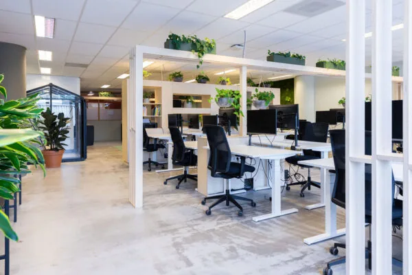 Moderne, open kantoorruimte aan de Johan Huizingalaan met witte bureaus, ergonomische stoelen en veel groene planten.