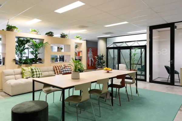 Modern ingerichte vergaderruimte aan de Johan Huizingalaan met een grote tafel, planten, een zithoek en glazen kantoorwanden.