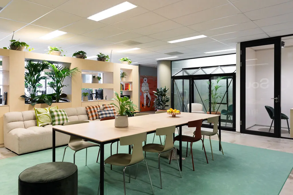 Modern ingerichte vergaderruimte aan de Johan Huizingalaan met een grote tafel, planten, een zithoek en glazen kantoorwanden.