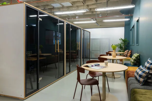 Moderne gezamenlijke werkruimte aan de Johan Huizingalaan met glazen vergaderruimtes, ronde tafels en kleurrijke kussens op een bank.