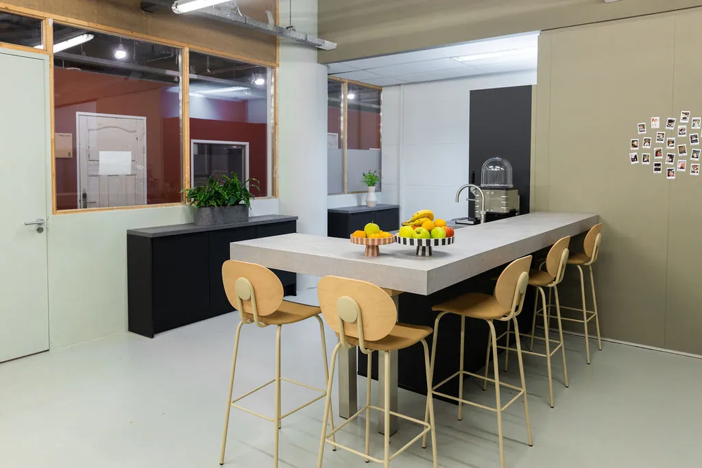 Moderne kantine aan de Johan Huizingalaan met hoge tafel, houten barkrukken en een schaal vers fruit.