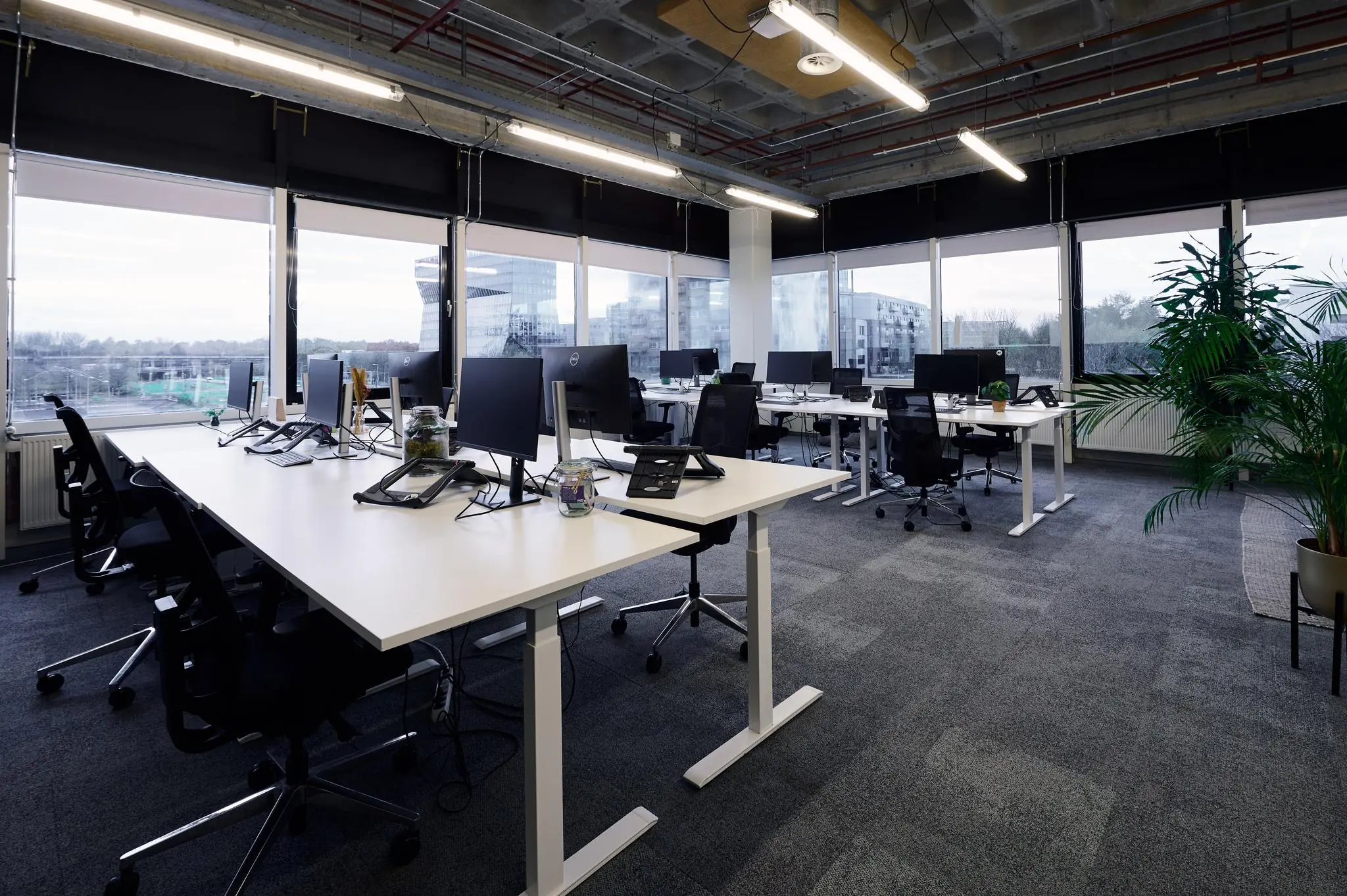 Modern kantoorinterieur aan de Johan Huizingalaan met verstelbare bureaus, computers en uitzicht op omliggende gebouwen.