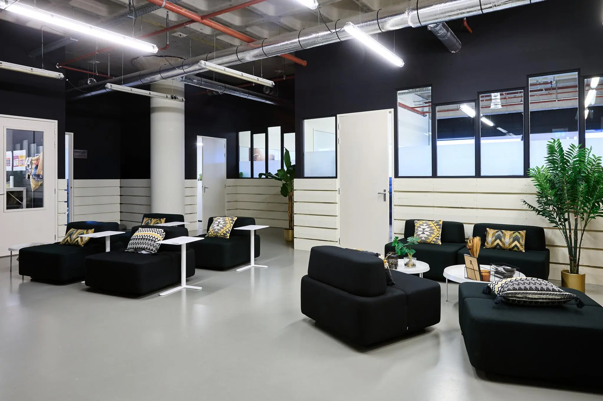 Moderne wachtruimte aan de Johan Huizingalaan met zwarte zitmeubels, kleurrijke kussens en industriële details.