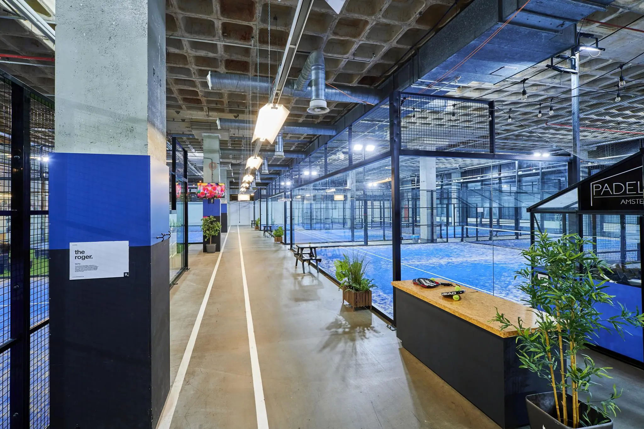 Binnenaanzicht van een moderne indoor padelhal aan de Johan Huizingalaan in Amsterdam met meerdere blauwgekleurde padelbanen.
