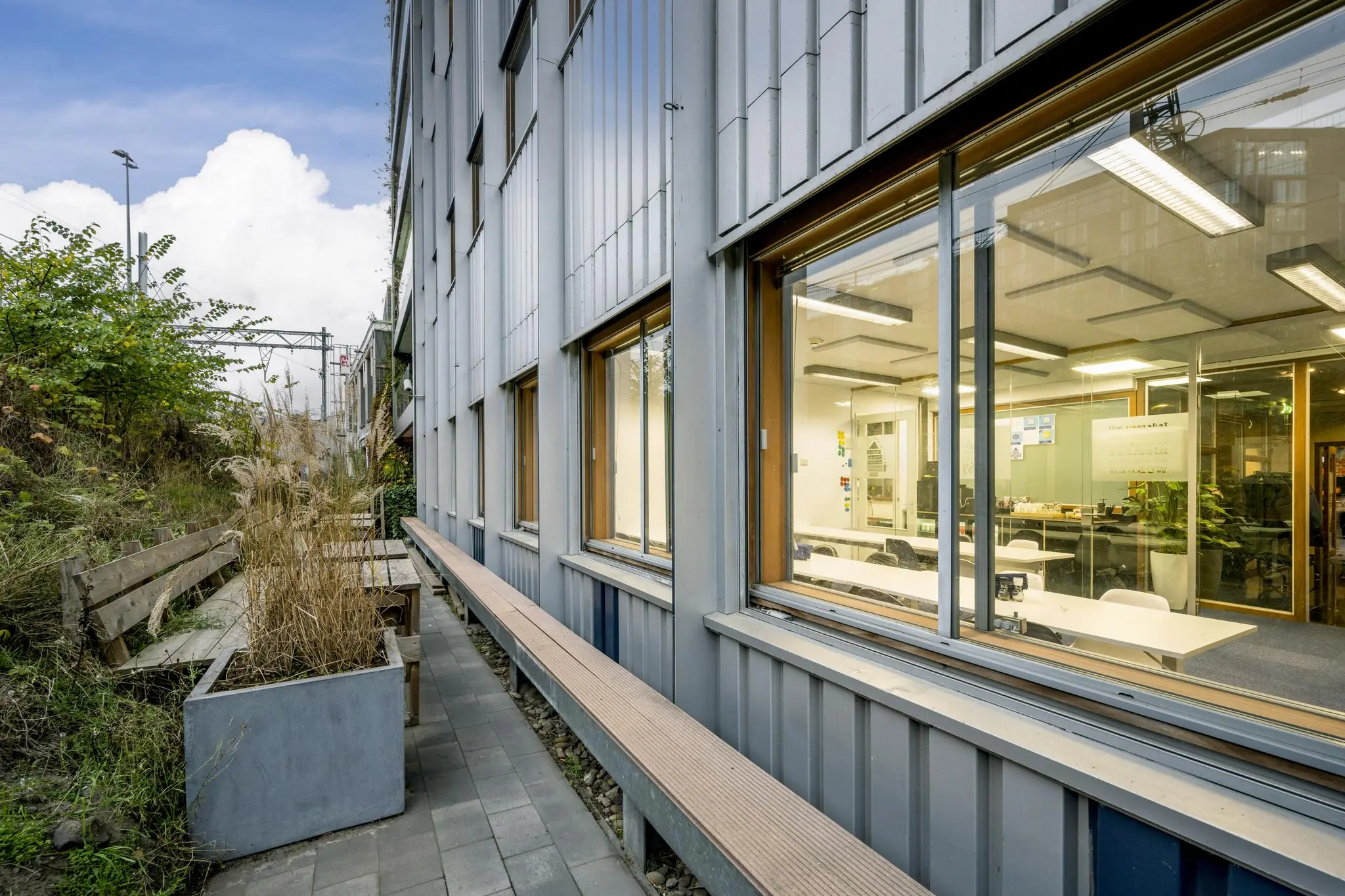 Buitenaanzicht van een modern kantoorpand aan de De Ruijterkade met zitplaatsen en planten naast het gebouw.