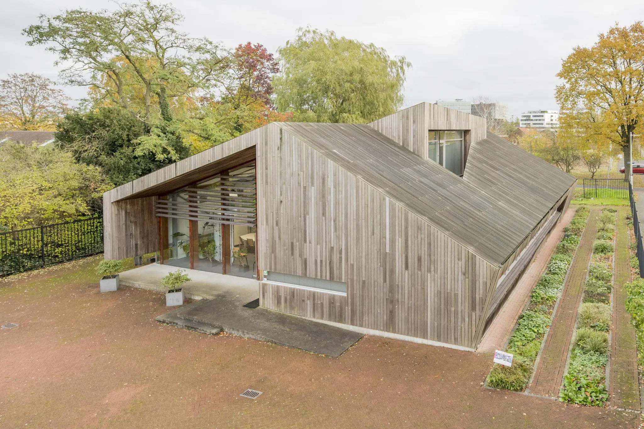 Modern houten gebouw met een schuin dak aan de Vogelvlinderweg, omringd door groen en tuinpaden.