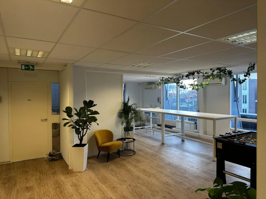 Modern kantoorinterieur aan de Koninginnegracht met hoge tafels, planten, een voetbaltafel en grote ramen met uitzicht op de stad.
