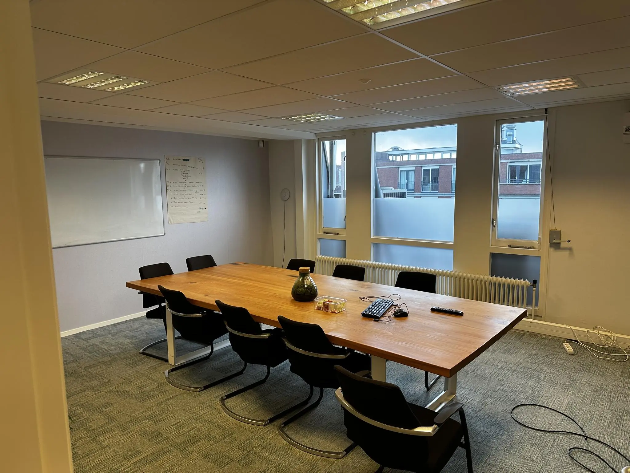 Vergaderruimte aan de Koninginnegracht met een grote houten tafel, acht stoelen, whiteboard en uitzicht op omliggende gebouwen.