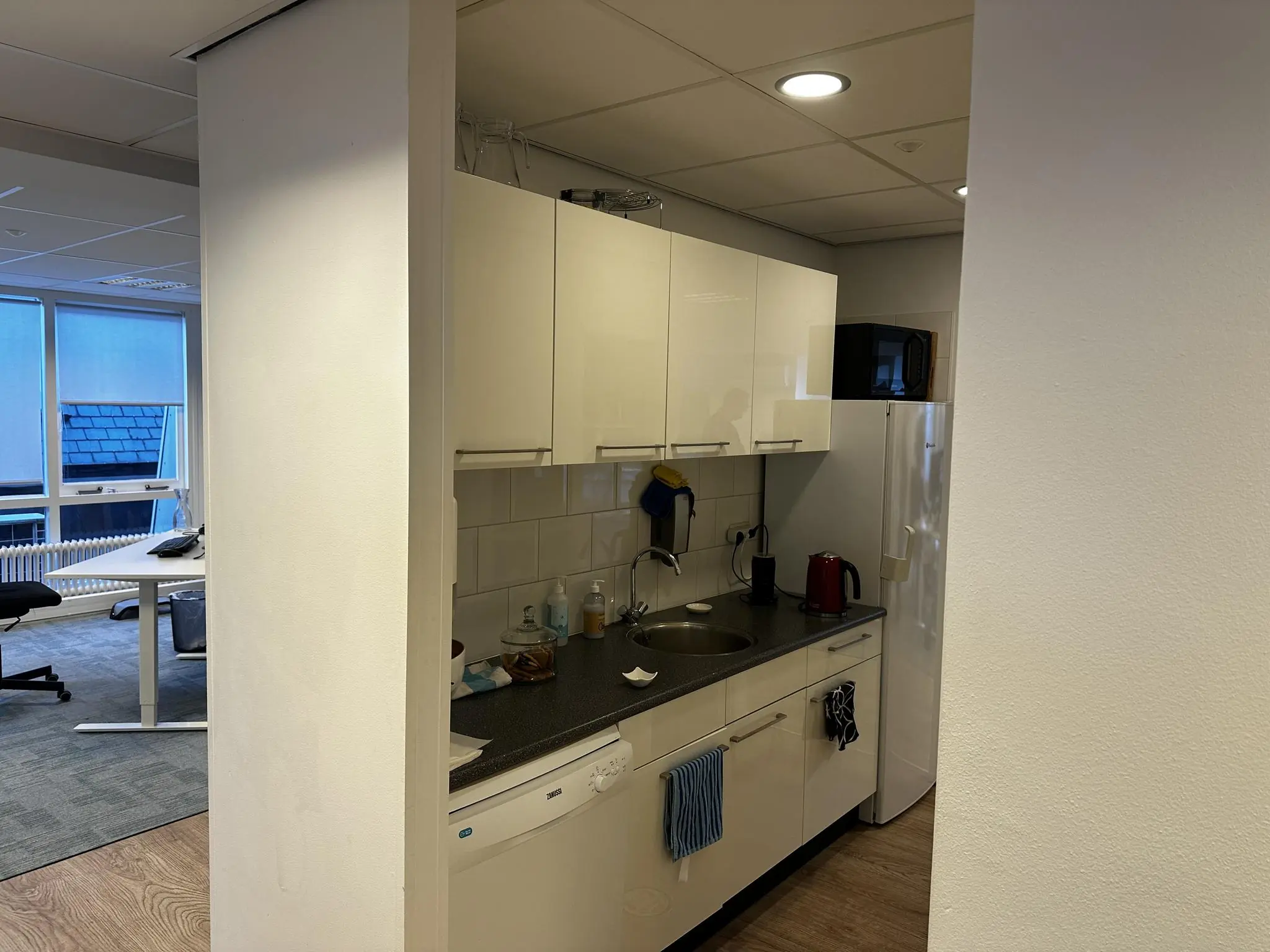Kleine kantoorkeuken aan de Koninginnegracht met witte kasten, koelkast en aanrecht met waterkoker.
