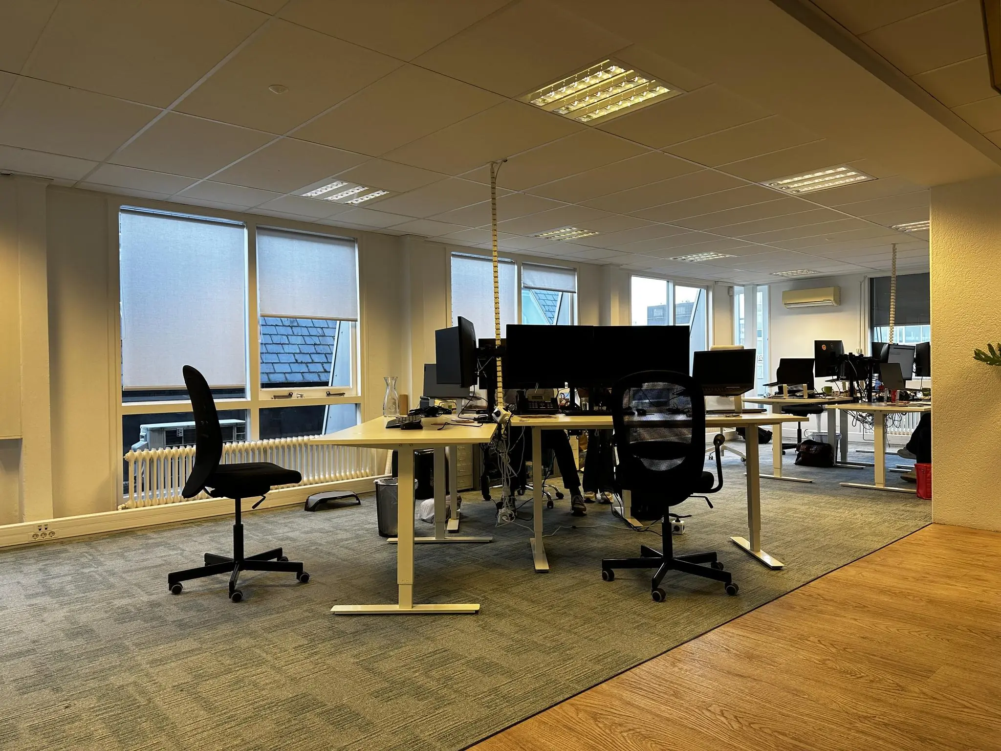 Moderne kantooruimte aan de Koninginnegracht met meerdere werkplekken, bureaustoelen en computeropstellingen.