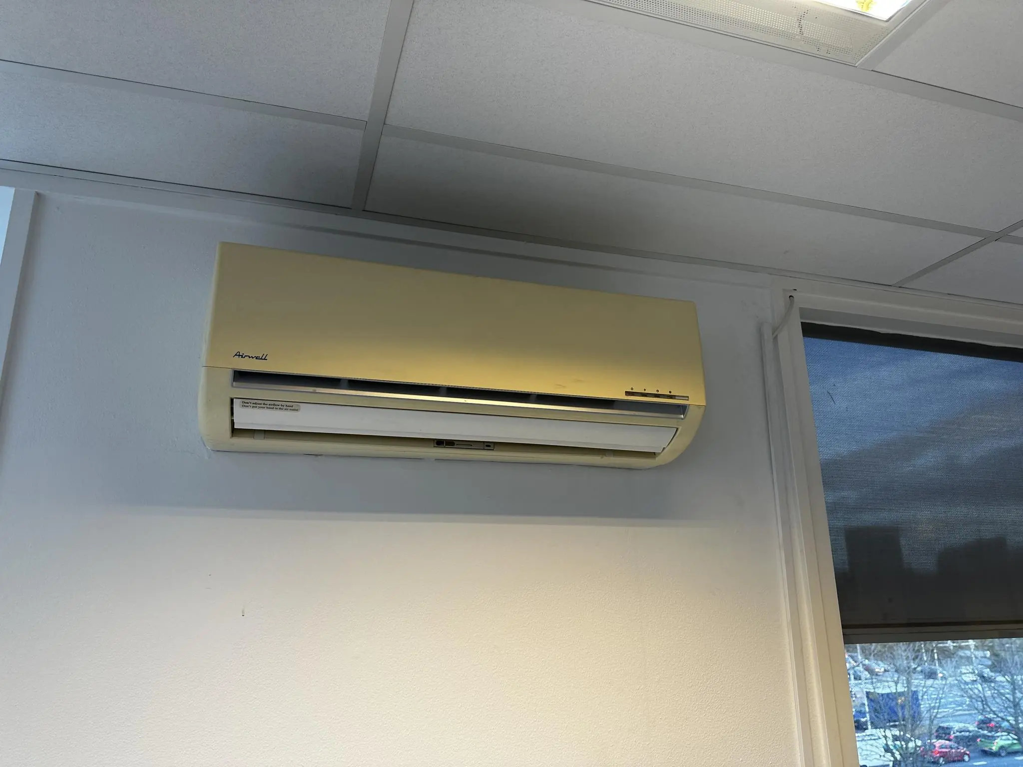 Vergeelde wandgemonteerde airco-unit van het merk Aermec aan een muur in een kantoorpand aan de Koninginnegracht.