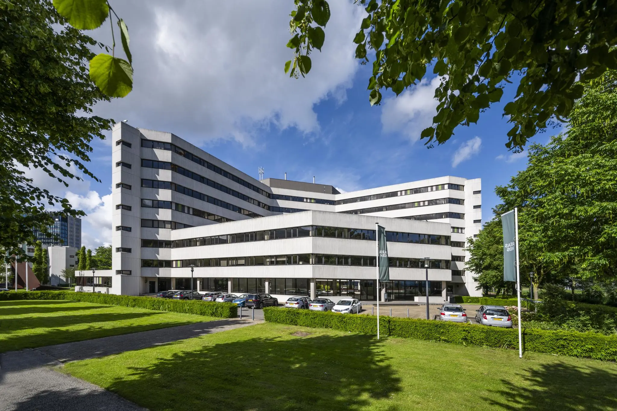 Modern kantoorgebouw aan de Hoogoorddreef in Amsterdam, omringd door groen en geparkeerde auto's.