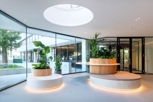 Moderne, lichtovergoten lobby van Hoogoorddreef met ronde zithoeken, plantenbakken en glazen wanden.
