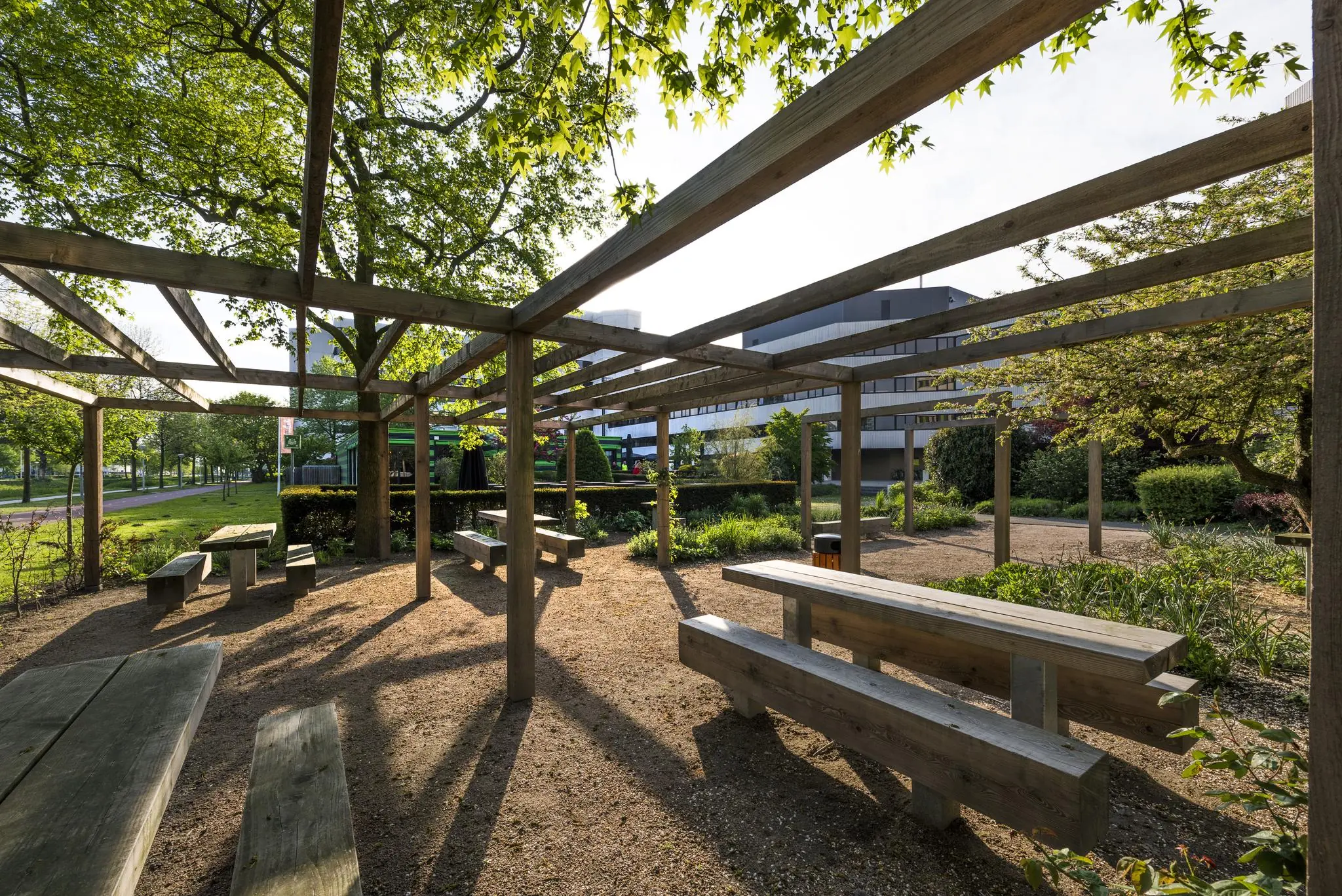 Overdekte zithoek met houten tafels en banken in een groene tuin aan de Hoogoorddreef.